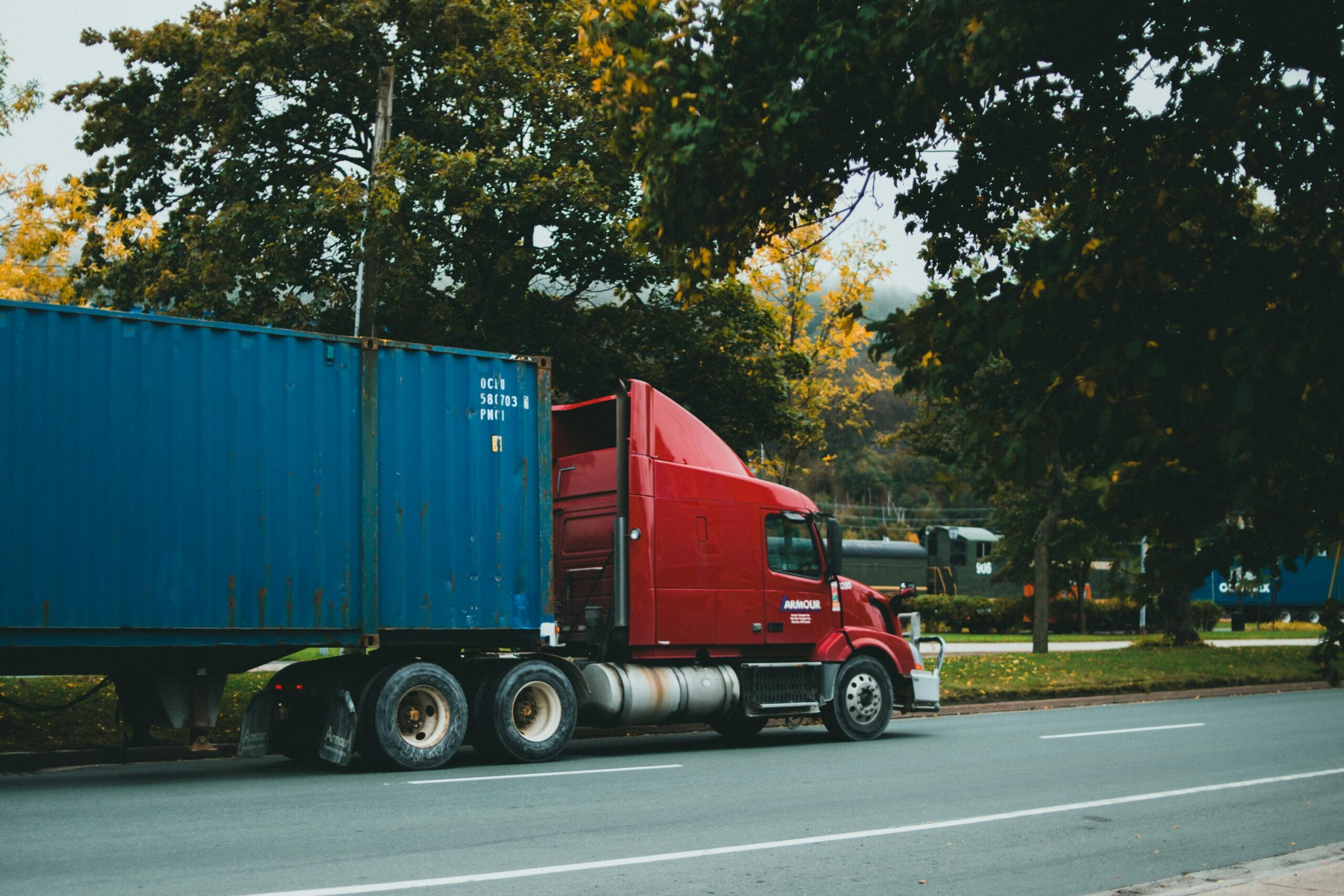 A red truck transports a blue cargo container on a scenic road,